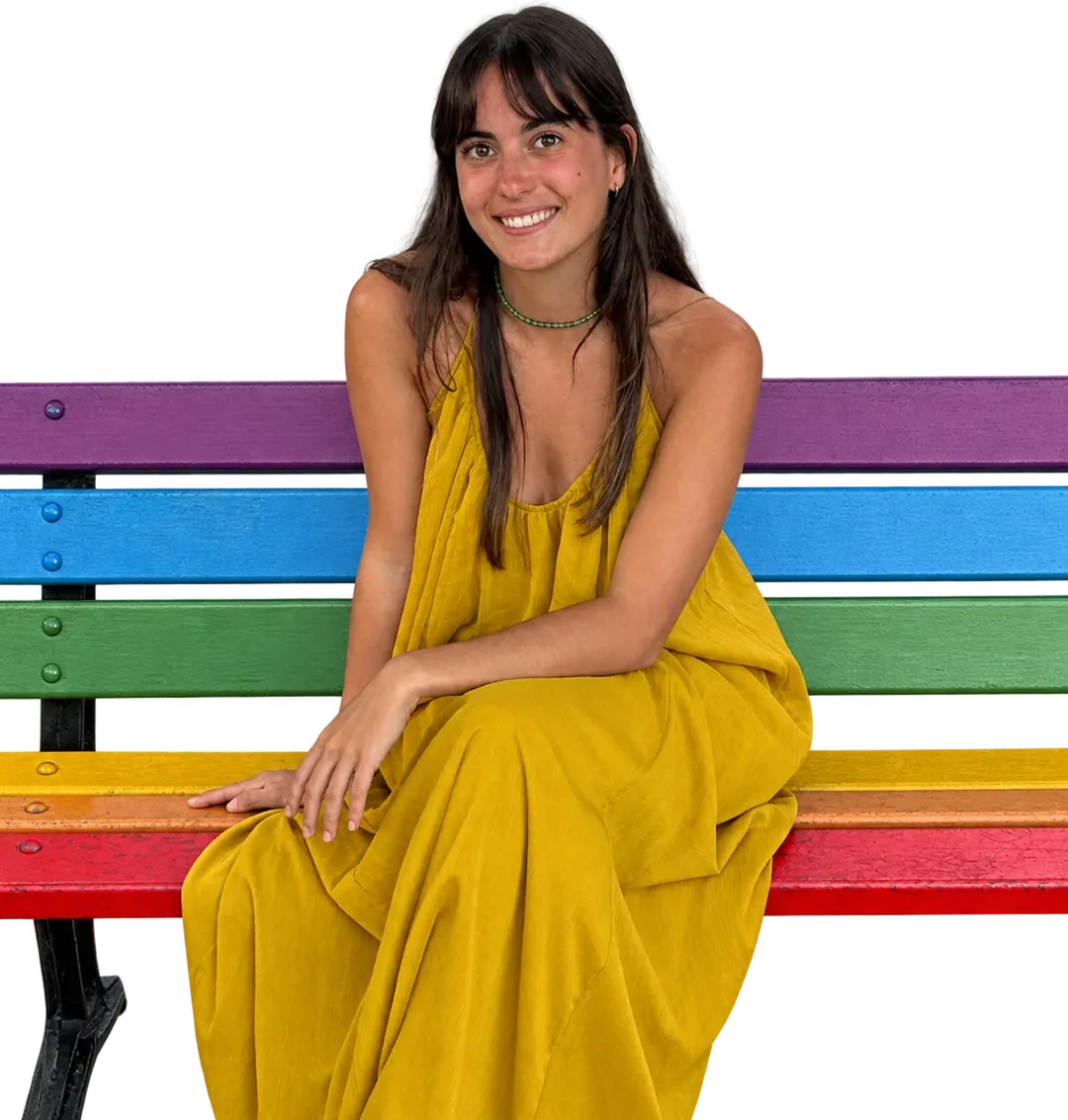 Belén Lovera sonríe sentada en un banco pintado con los colores del arcoíris.